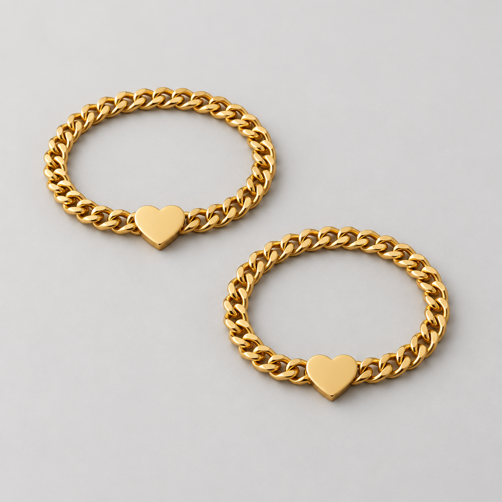 Two hands holding each other wearing gold bracelets with heart charms on a warm-toned background.