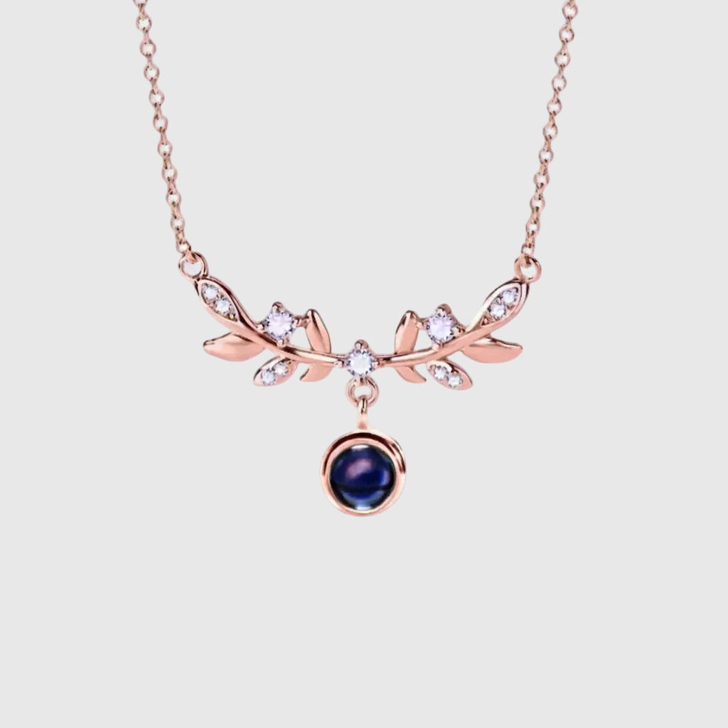 Rose gold necklace with leaf design and blue gemstone, featuring a photo pendant of a couple and baby.